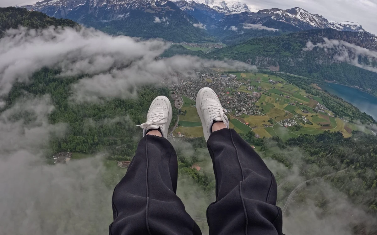 A passenger view of boots hanging in a harness above a green valley floor