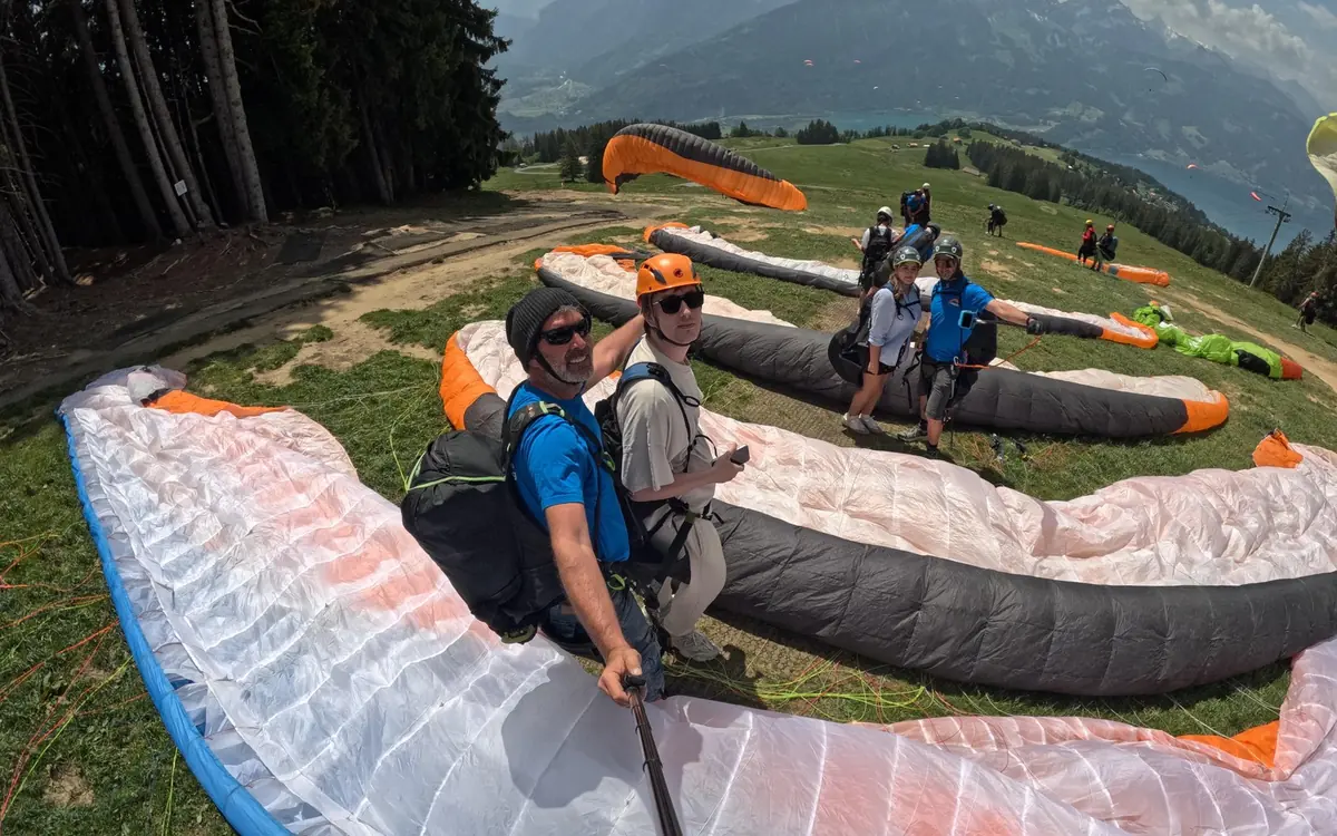 A tandem pair standing on a grassy launch slope with the wing spread behind them