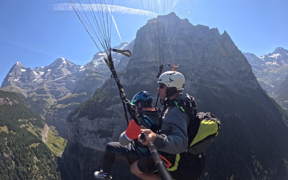 A paraglider above the vertical cliffs of a deep valley with waterfalls on the far wall