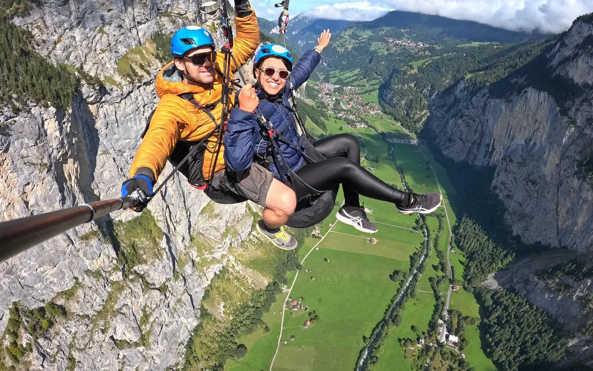 Two people under one tandem paraglider wing above an alpine valley