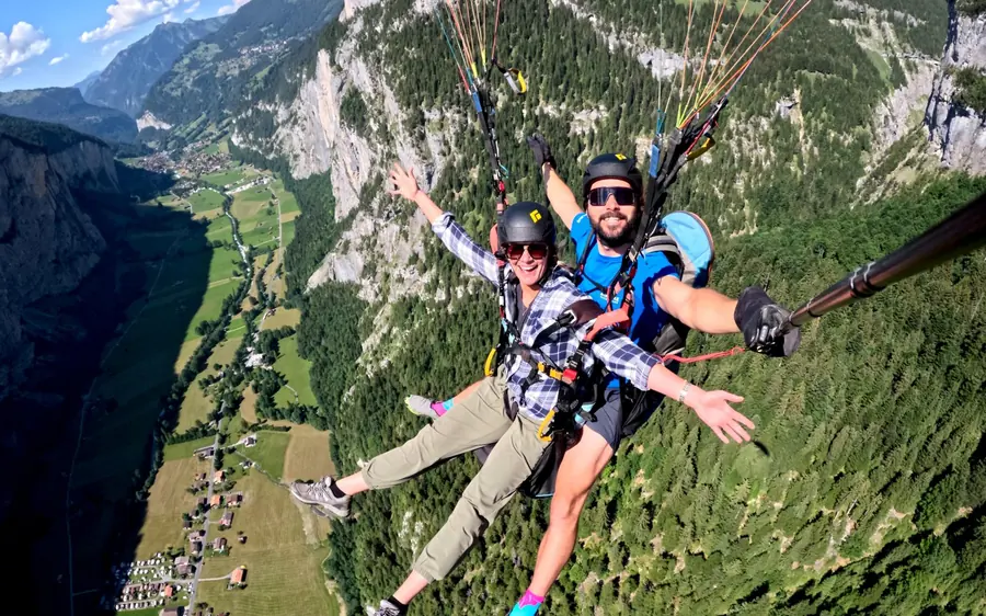 A tandem paraglider high above the walls and waterfalls of an alpine valley